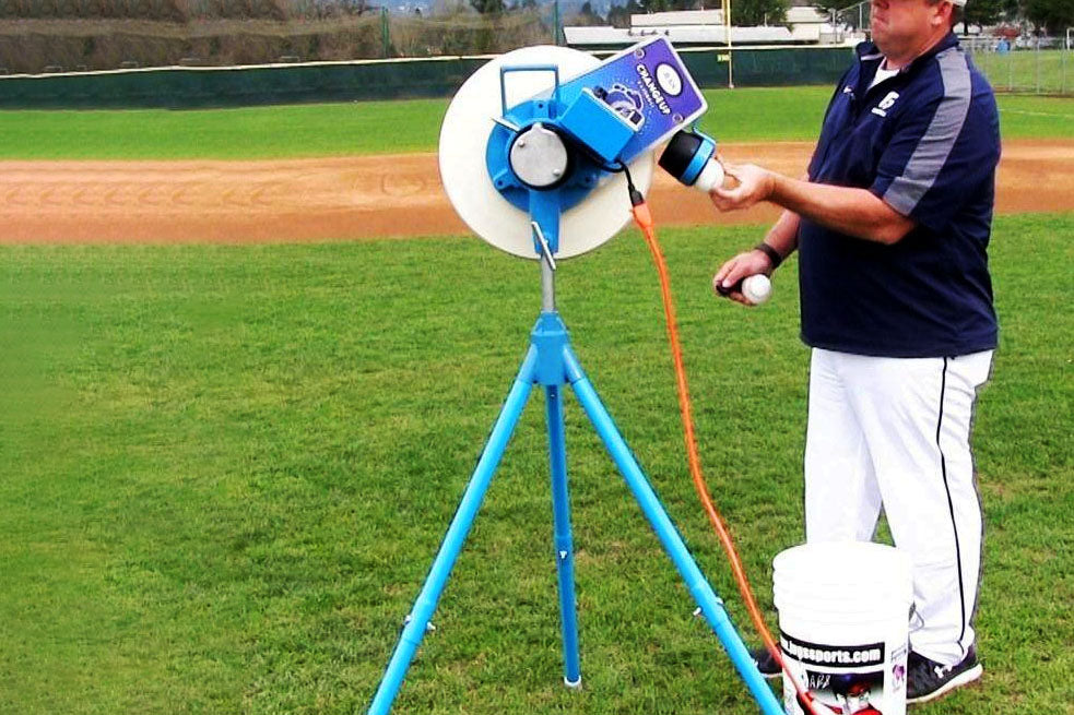 Staff member loading baseballs into a JUGS Changeup pitching machine on a baseball field