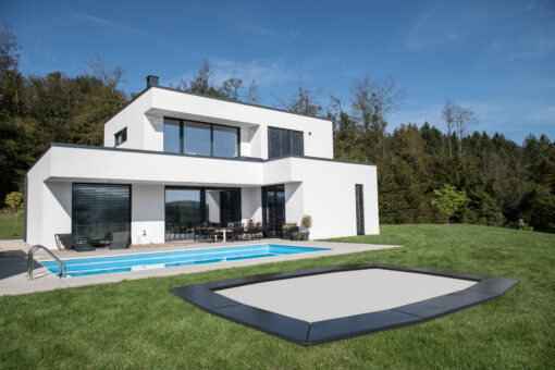 In-ground rectangular trampoline installed flush with a manicured green lawn in front of a modern two-story house
