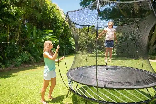 Girl jumping on Springfree Compact Round Trampoline with adult supervising